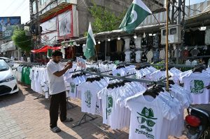 A vendor displays Pakistani flags, badges, headbands and other Jashn-e-Azadi items at a roadside stall near Commercial Market as shoppers browse the festive merchandise ahead of Independence Day celebrations