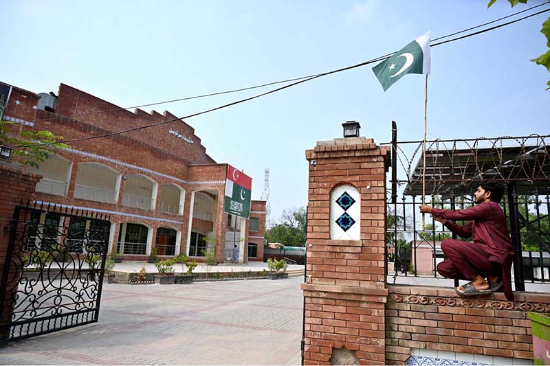 A man installs Pakistani national flags on the Arts Council building ahead of Independence Day celebrations
