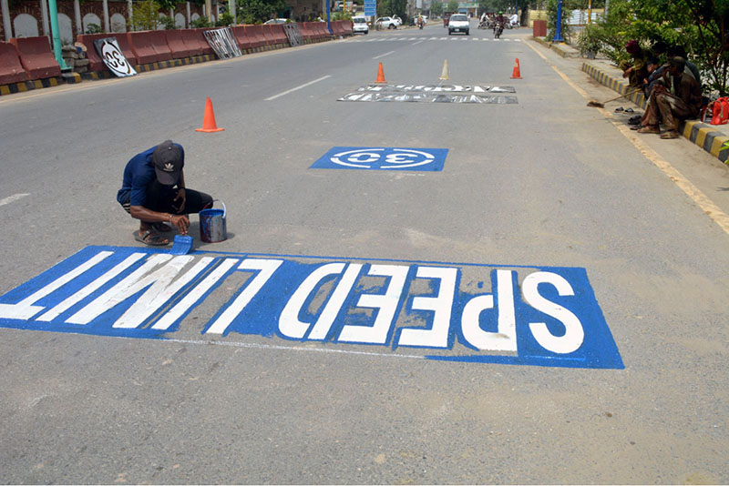 A worker paints road signs along Jail Road as part of routine maintenance work in the city
