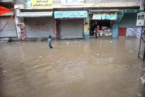 A child stands amid floodwater as an auto-rickshaw makes its way through the inundated street following heavy monsoon rains in Dhoke Khabba