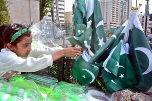 A girl vendor arranges Pakistani national flags in a basket to attract customers ahead of Independence Day celebrations