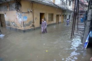 A child stands amid floodwater as an auto-rickshaw makes its way through the inundated street following heavy monsoon rains in Dhoke Khabba