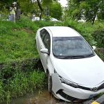 A car slips from a parking area and falls into a roadside drain in front of the Excise Office