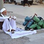 An elderly vendor patiently waits for customers to sell plastic ewers on roadside at Maghanki Road