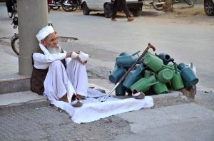 An elderly vendor patiently waits for customers to sell plastic ewers on roadside at Maghanki Road