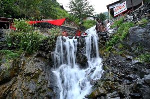 Tourists enjoy the scenic beauty of Miran Jani Water Fall, where cascading water flows through lush green surroundings, providing a refreshing retreat for visitors.