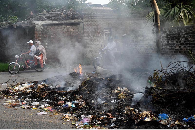 People rides past as smoke billows from a burning garbage dump in residential areas Railway Colony posing a serious threat to human health and the environment ,to attention the concern authorities