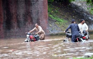 Train passes over a bridge as vehicles lie stranded in deep floodwater below, following heavy monsoon rain at Rahimabad area in the City.