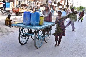 A gypsy woman walks with her daughter, pushing a handcart after collecting clean water from a water source along Subzi Mandi Road.