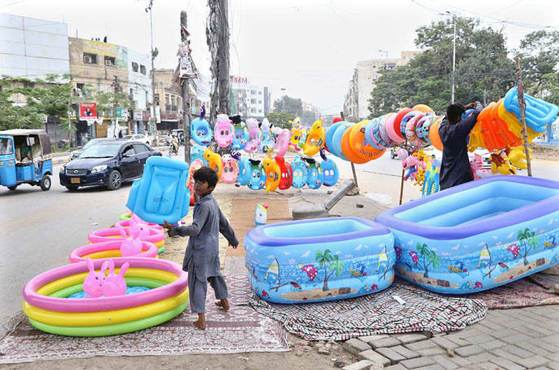 A vendor arranges inflatable swimming pools, toys and other children’s items for sale at a roadside his setup