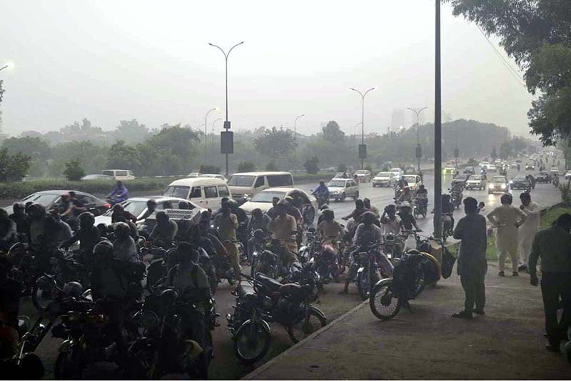 Pedestrians and motorcyclists take shelter under the Srinagar Highway bridge to escape heavy rain in the federal capital