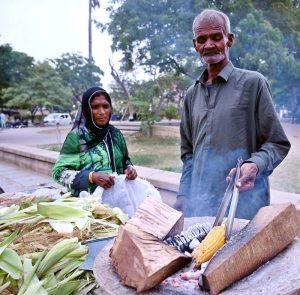 A vendor family sells roasted corn at a park to attract customers.