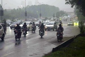 Pedestrians and motorcyclists take shelter under the Srinagar Highway bridge to escape heavy rain in the federal capital