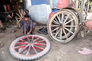 Artisans repair and assemble wooden wheels for traditional horse-drawn carts at a roadside workshop.