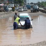 People push a car that broke down after becoming stranded in rainwater on a service road