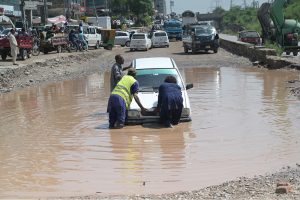 People push a car that broke down after becoming stranded in rainwater on a service road