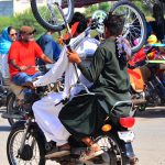 A youngster holds a bicycle while sitting on the rear seat of a motorcycle