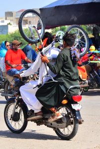 A youngster holds a bicycle while sitting on the rear seat of a motorcycle