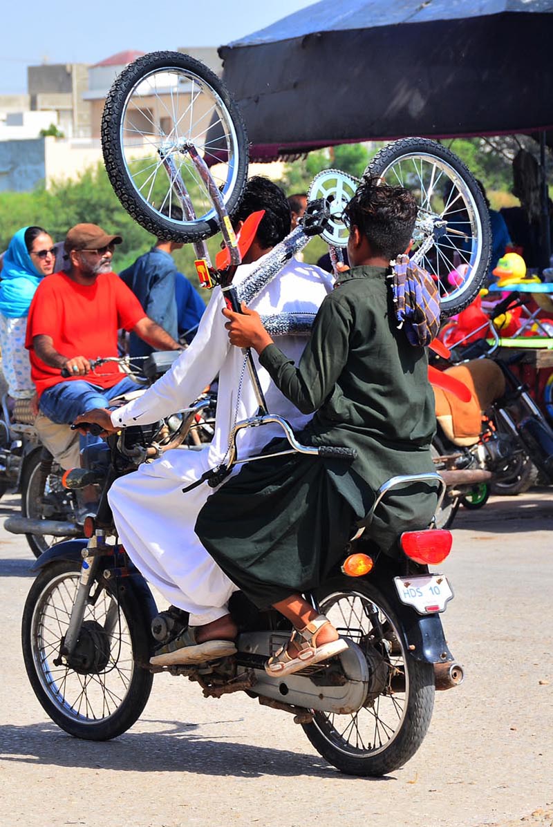 A youngster holds a bicycle while sitting on the rear seat of a motorcycle