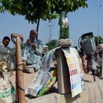 Daily-wage labourers sit on a green belt with their tools while eating bread and waiting for customers at PWD area in the Federal Capital