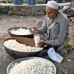 An elderly vendor is busy packing popcorn into plastic bags for sale on Kuuri Road