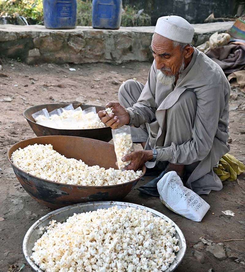 An elderly vendor is busy packing popcorn into plastic bags for sale on Kuuri Road