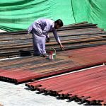 A worker painting iron scaffolding pipes, used in building construction, at a construction site