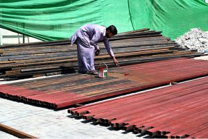 A worker painting iron scaffolding pipes, used in building construction, at a construction site