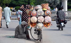 A vendor sits beside his bicycle loaded with colourful handwoven baskets, displayed for sale