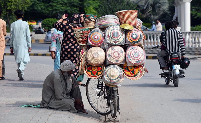 A vendor sits beside his bicycle loaded with colourful handwoven baskets, displayed for sale