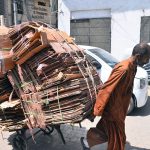 A labourer pushes a wheelbarrow loaded with cardboard boxes along Saddar Road