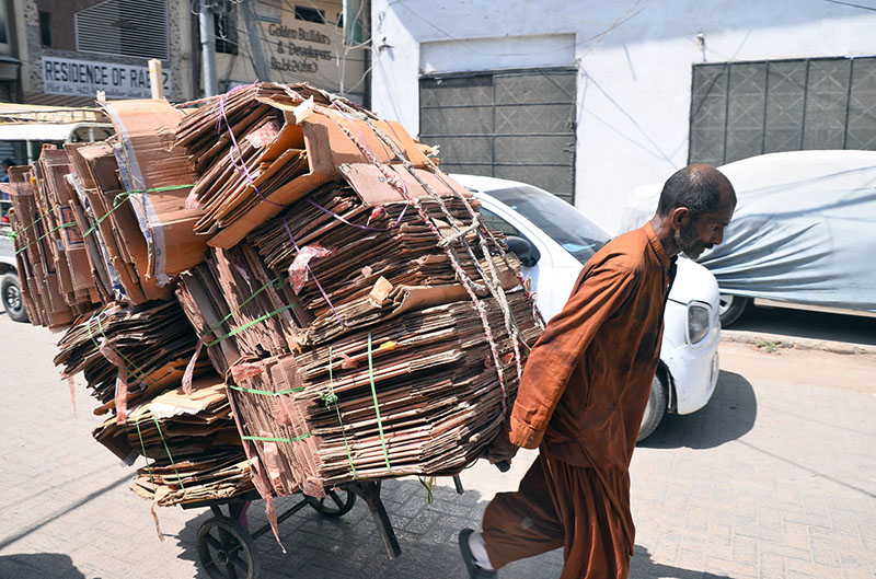 A labourer pushes a wheelbarrow loaded with cardboard boxes along Saddar Road