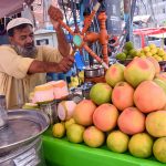 A vendor operates a manual juicer to prepare fresh fruit juice at his stall