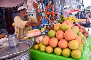 A vendor operates a manual juicer to prepare fresh fruit juice at his stall