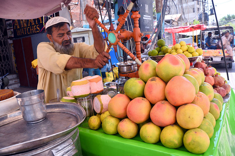 A vendor operates a manual juicer to prepare fresh fruit juice at his stall