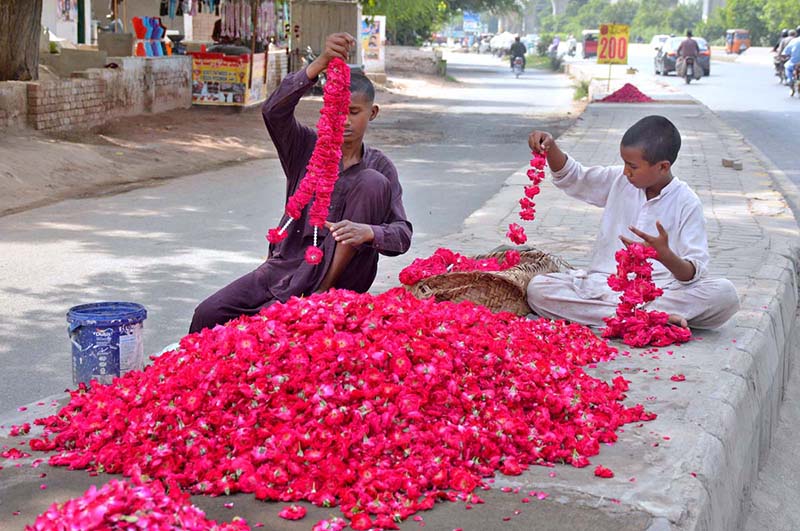 Young vendors prepare red rose garlands along the roadside to attract customers