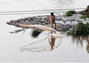 A man casts a fishing net into Rawal Lake
