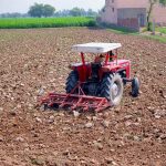 A farmer drives a tractor equipped with a cultivator through a field during land preparation for the next crop, as egrets forage behind the farm machinery