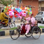 An elderly person with a disability displays colourful inflatable toys on his tricycle while selling them along a roadside to earn a livelihood