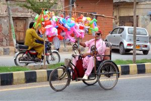 An elderly person with a disability displays colourful inflatable toys on his tricycle while selling them along a roadside to earn a livelihood