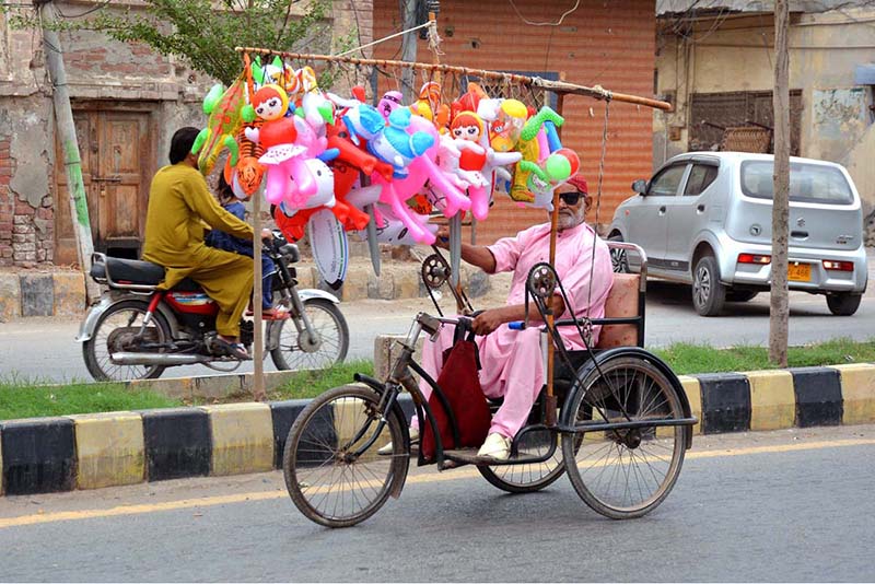 An elderly person with a disability displays colourful inflatable toys on his tricycle while selling them along a roadside to earn a livelihood