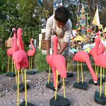A boy displays handmade pink flamingo garden statues outdoors to attract customers