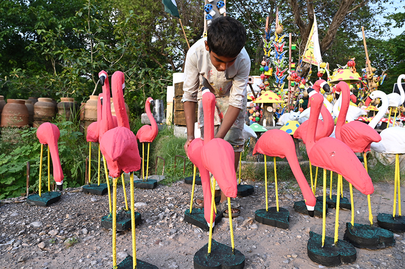 A boy displays handmade pink flamingo garden statues outdoors to attract customers