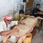 Artisans weave cane mesh onto traditional wooden furniture frames at a workshop at Dhok Kala Khan