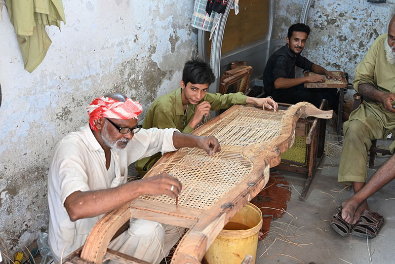 Artisans weave cane mesh onto traditional wooden furniture frames at a workshop at Dhok Kala Khan