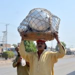 A man transports silver crockery on his head while walking along a road to sell it