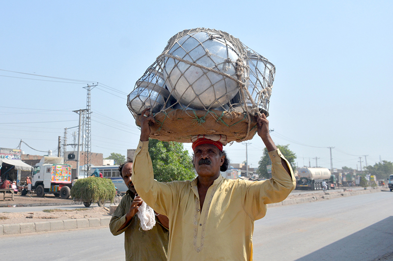 A man transports silver crockery on his head while walking along a road to sell it