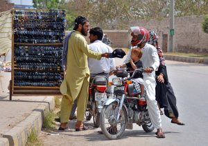 A roadside vendor sells a variety of sunglasses and caps to motorcyclists to earn a livelihood.