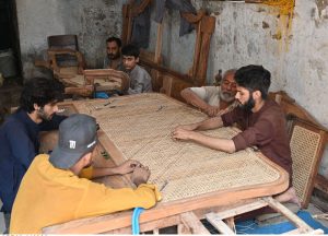 Artisans weave cane mesh onto traditional wooden furniture frames at a workshop at Dhok Kala Khan