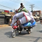 A labourer sitting on luggage loaded on a tricycle loader, while the driver is busy with his cell phone, may cause a mishap